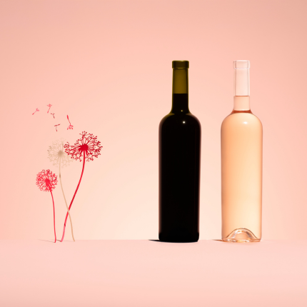 Une bouteille en verre vert Antique pour vin rouge et une bouteille en verre blanc pour vin rosé de la gamme Optimum, à côté de pissenlits stylisés sur fond rose.