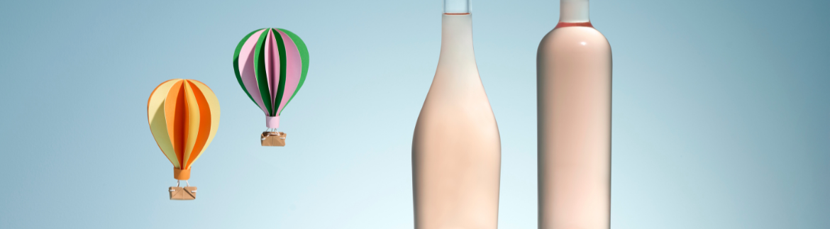 Deux bouteilles en verre blanc de formes différentes pour vin rosé, à côté de deux montgolfières colorées en papier sur un fond bleu pastel.